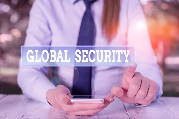 Handwriting text Global Security. Conceptual photo protection of the world against war and other threats Female business person sitting by table and holding mobile phone