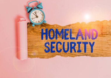 Word writing text Homeland Security. Business photo showcasing federal agency designed to protect the USA against threats Alarm clock and torn cardboard placed above a wooden classic table backdrop