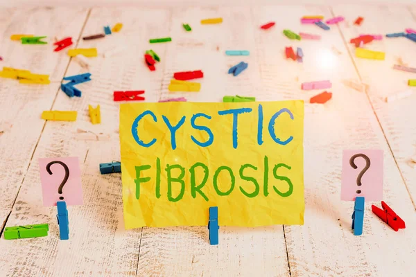 Conceptual hand writing showing Cystic Fibrosis. Concept meaning a hereditary disorder affecting the exocrine glands Crumbling sheet with paper clips placed on the wooden table