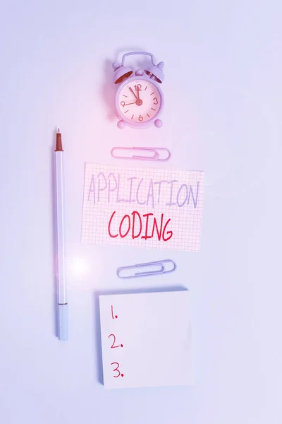 Conceptual hand writing showing Application Coding. Business photo text process by which a mobile app is developed for mobile Alarm clock squared paper notepad marker clips colored background.