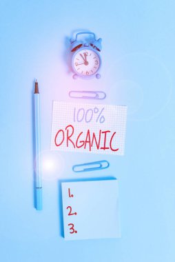 Conceptual hand writing showing 100 Percent Organic. Concept meaning ingredients are certified no artificial food additives Alarm clock squared paper notepad marker clips colored background