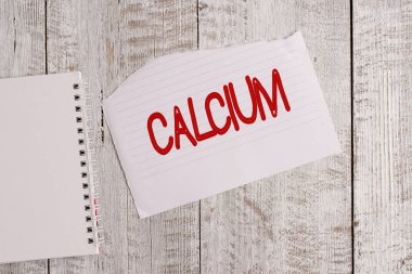 Kalsiyum gösteren kavramsal el yazısı. İş fotoğrafı metni insan vücudundaki en çok bulunan beşinci element gümüş beyazı metal kağıt ve defter levhası klasik ahşap masa üzerine yerleştirilmiş..