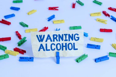 El yazısı Alkol Uyarı metni. Alkollü içeceklerin ambalajında mesajların görünmesi kavramı Renkli çamaşır iğnesi kağıtları boş hatırlatıcı beyaz zemin arka plan ofisi.