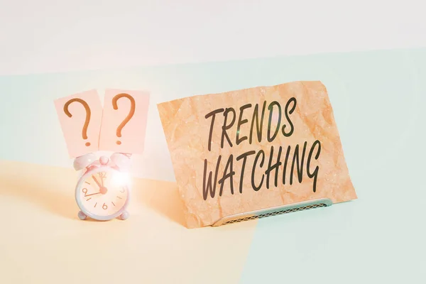 Word writing text Trends Watching. Business concept for change or development towards something new or different Mini size alarm clock beside a Paper sheet placed tilted on pastel backdrop.