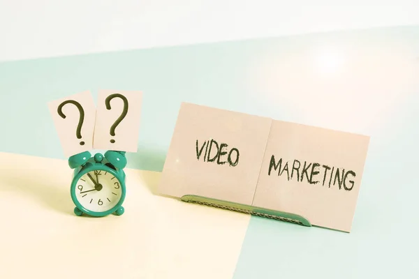 Word writing text Video Marketing. Business concept for integrates engaging video into the marketing campaigns Mini size alarm clock beside a Paper sheet placed tilted on pastel backdrop.