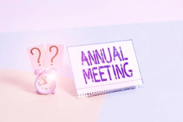 Text sign showing Annual Meeting. Conceptual photo a meeting of the general membership of an organization Mini size alarm clock beside a Paper sheet placed tilted on pastel backdrop.