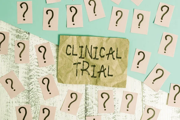 Word writing text Clinical Trial. Business concept for trials to evaluate the effectiveness and safety of medication Scribbled and crumbling papers with thick cardboard above wooden table.