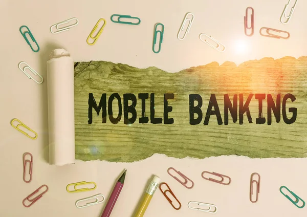 Text sign showing Mobile Banking. Conceptual photo use of cellular device to perform online banking tasks Stationary and torn cardboard placed above a wooden classic table backdrop.