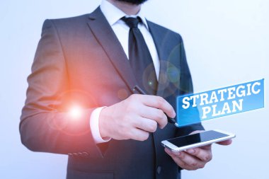 Stratejik Planı gösteren metin işareti. Öncelikleri belirlemek ve odaklamak için kullanılan kavramsal fotoğraf analiz etkinliği. Erkek giyimi resmi iş kıyafeti. Akıllı yüksek teknoloji akıllı telefon kullan..
