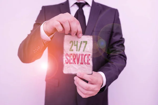 Handwriting text 24 Or 7 Service. Concept meaning service that is available any time and usually every day Male human wear formal work suit office look hold notepaper sheet use hand. — Stock Photo, Image