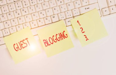 Handwriting text Guest Blogging. Concept meaning used by the owners of blogs to increase traffic to their site Three empty green square papers by the pc keyboard with copy space.