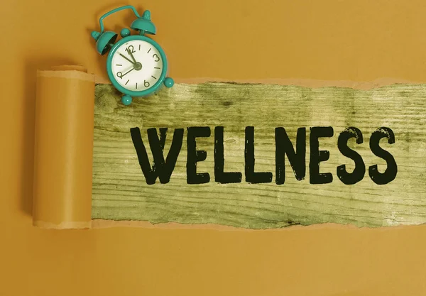 Handwriting text writing Wellness. Concept meaning state of being in good health especially as actively pursued goal Alarm clock and torn cardboard placed above a wooden classic table backdrop. — Stock Photo, Image