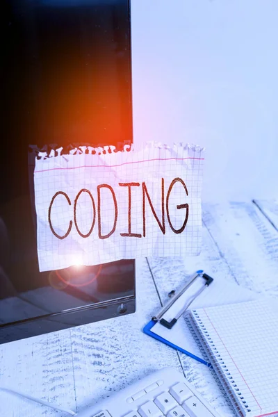 Handwriting text Coding. Concept meaning assigning code to something for classification identification Note paper taped to black computer screen near keyboard and stationary.