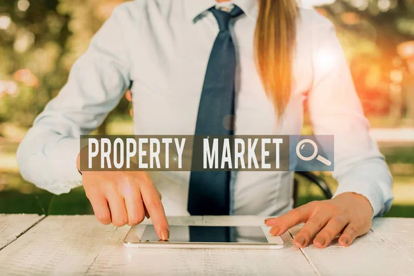 Writing note showing Property Market. Business photo showcasing the buying and selling of land and buildings Estate market Female business person sitting by table and holding mobile phone. — Stockfoto