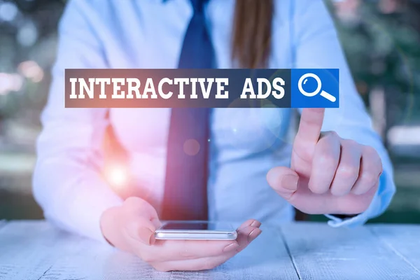 Text sign showing Interactive Ads. Conceptual photo uses interactive media to communicate with consumers Female business person sitting by table and holding mobile phone. — Stock Photo, Image