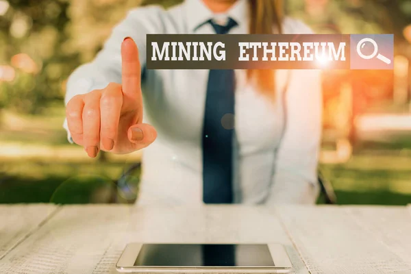 Word writing text Mining Ethereum. Business concept for the process of increasing the volume of Ether in circulation Female business person sitting by table and holding mobile phone.