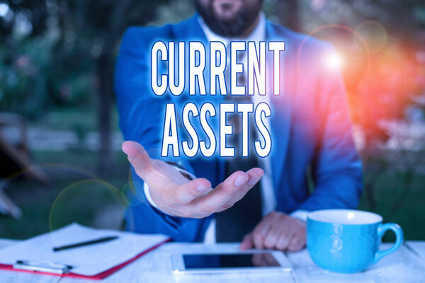 Word writing text Current Assets. Business concept for any asset which can reasonably be expected to be sold Man with opened hands in fron of the table. Mobile phone and notes on the table.