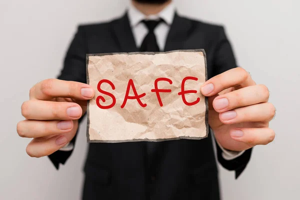 Word writing text Safe. Business concept for protected from or not exposed to danger or risk Not likely to be harmed Male human wear formal work suit office look hold notepaper sheet use hand. — Stockfoto