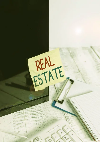 Writing note showing Real Estate. Business photo showcasing the property consisting of land and the buildings on it Note paper taped to black computer screen near keyboard and stationary. — Stock fotografie