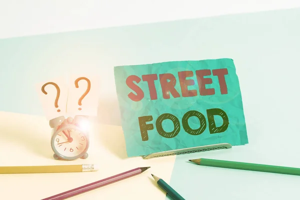 Kata menulis teks Street Food. Konsep bisnis untuk makanan yang dimasak dijual oleh pedagang di jalan atau di tempat umum lainnya Jam alarm ukuran kecil di samping stasioner yang diletakkan miring di latar belakang pastel . — Stok Foto