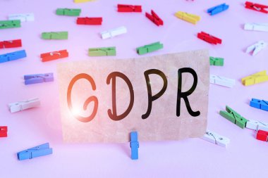 GDPR 'ı gösteren kavramsal el yazısı. İş fotoğrafı metni düzenlemesi, göstermelik verileri ve vatandaşların mahremiyetini koruyor. Renkli çamaşır iğnesi kağıtları boş, pembe zemin ofis broşu..