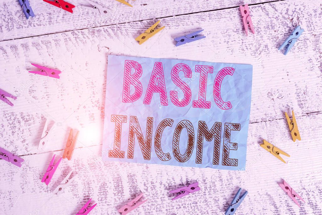 Writing note showing Basic Income. Business photo showcasing periodic cash payment unconditionally delivered Minimum income Colored clothespin rectangle square shaped paper white wood background.