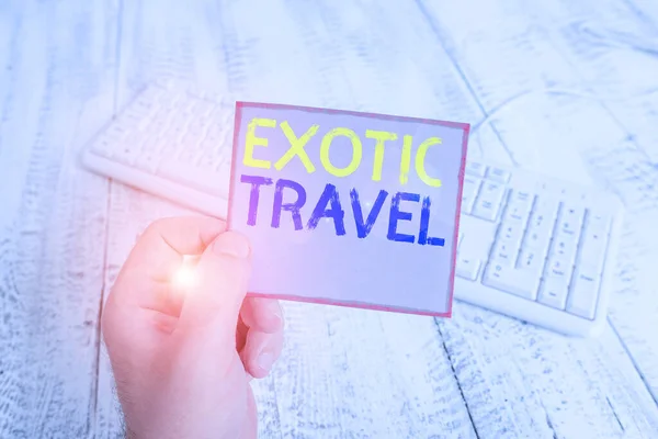 Word writing text Exotic Travel. Business concept for Travelling to unusual places or unfamiliar destination man holding colorful reminder square shaped paper white keyboard wood floor. — ストック写真