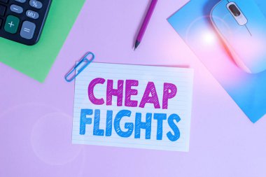 Ucuz uçuşları gösteren bir not yazıyorum. Ticari fotoğraf gösteriminin maliyeti az ya da daha az, normal ya da beklenenden daha az, elektronik fare hesap makinesi kağıt kağıtları, ataç rengi arka plan.