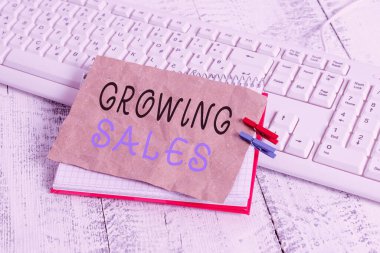 Handwriting text writing Growing Sales. Concept meaning Average sales volume of a company products has grown notebook paper reminder clothespin pinned sheet white keyboard light wooden.