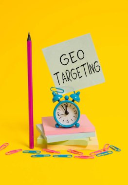 Coğrafi Hedefleme 'yi gösteren bir not yazıyorum. Bir web sitesi ziyaretçisinin coğrafi konumunu belirlemek için iş fotoğrafı gösterme yöntemi. Alarm saati yapış yapış not defterleri kalem renkli arkaplan.