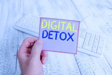 Kelime yazma metni Dijital Detox. Bir gösteri sırasında iş kavramı, elinde renkli hatırlatıcı kare şeklindeki kağıt beyaz klavye ahşap zemin tutan aletleri kullanmayı durdurur..
