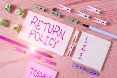 İade Politikasını gösteren bir not yazıyorum. Renkli çamaşır iğnesi kağıtları boş ahşap zemin ofisini hatırlatmadan önce iş fotoğraflarının geri dönüşünü veya kusurlu ürünleri takas ederler..