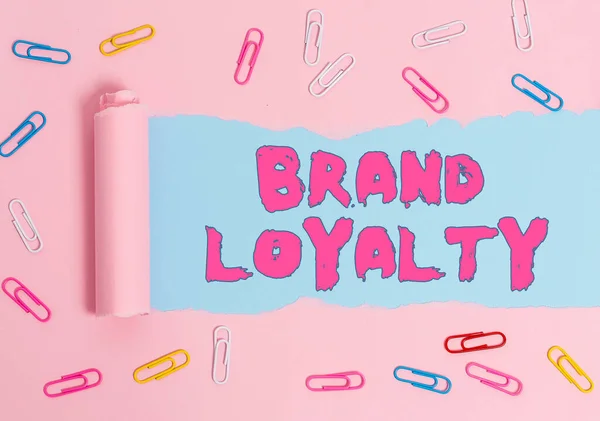 Word writing text Brand Loyalty. Business concept for Dedication to purchase the same product or service repeatedly Paper clip and torn cardboard placed above a plain pastel table backdrop.