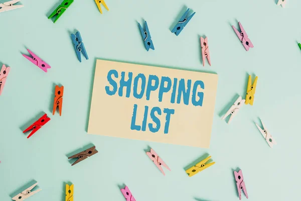 Conceptual hand writing showing Shopping List. Business photo text a list of items to be considered or purchases to be made Colored clothespin rectangle shaped paper blue background.