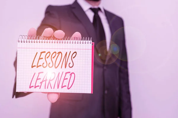 Text sign showing Lessons Learned. Conceptual photo the knowledge or understanding gained by experience Male human wear formal work suit office look hold mathematics book use hand. — Stockfoto