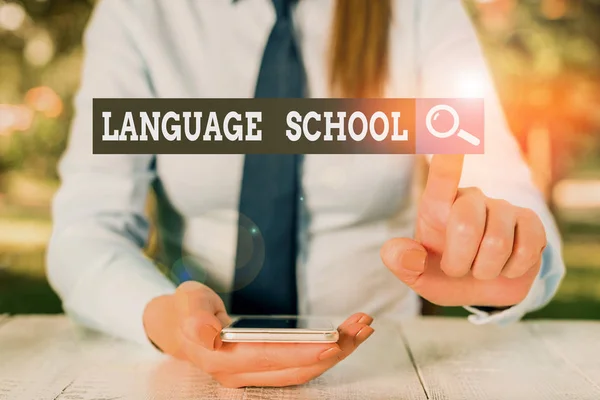 Text sign showing Language School. Conceptual photo educational institution where foreign languages are taught Female business person sitting by table and holding mobile phone.