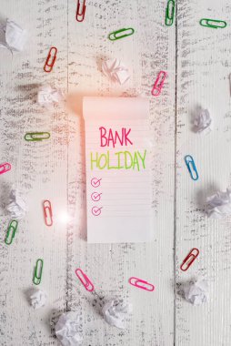 Conceptual hand writing showing Bank Holiday. Business photo showcasing A day on which banks are officially closed as a public holiday Stripped ruled notepad clips paper balls wooden background. clipart
