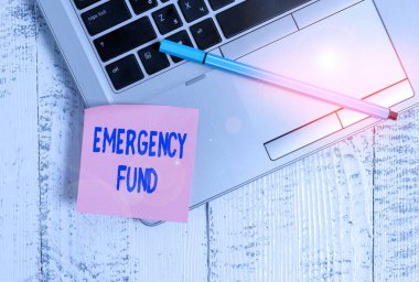 Handwriting text Emergency Fund. Concept meaning Money which is set aside for an emergency situation Trendy slim silver metallic laptop blank sticky pad pen lying vintage table.