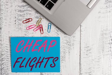 Ucuz uçuşları gösteren bir not yazıyorum. İş fotoğraflarının maliyeti az ya da daha az. Trendi metalik dizüstü bilgisayar boş renkli klipsleri klasik masa üzerinde..