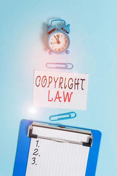 Word writing text Copyright Law. Business concept for body of law that governs the original works of authorship Alarm clock clipboard squared blank paper sheet clips colored background.