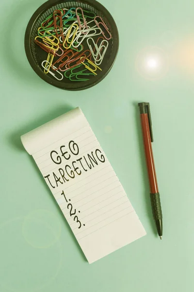Conceptual hand writing showing Geo Targeting. Business photo text method of determining the geolocation of a website visitor Notebook and stationary with mouse above pastel backdrop.