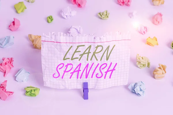 Handwriting text writing Learn Spanish. Concept meaning gain or acquire knowledge of speaking and writing Spanish Colored crumpled papers empty reminder white floor background clothespin.