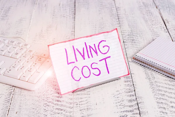 Conceptual hand writing showing Living Cost. Business photo showcasing the amount of money that a demonstrating needs to sustain life Notepaper on wire in between computer keyboard and sheets. — Stockfoto