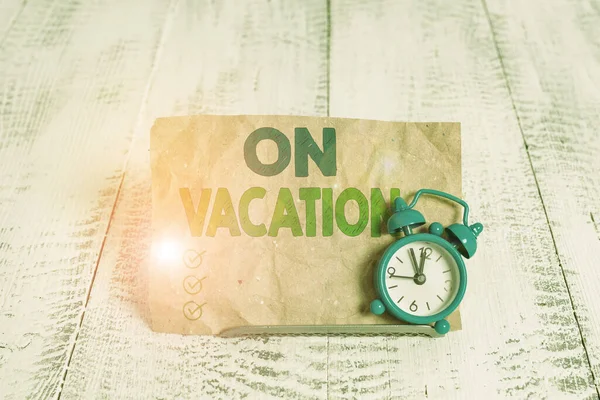 书写关于假期的文字。概念意思是在旅行或娱乐中离开家或出差的时间。微型蓝色闹钟停在笔记本前的缓冲线上方. — 图库照片