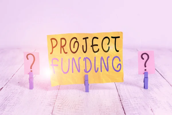 Writing note showing Project Funding. Business photo showcasing capital required to undertake a project or programme Crumbling sheet with paper clips placed on the wooden table.