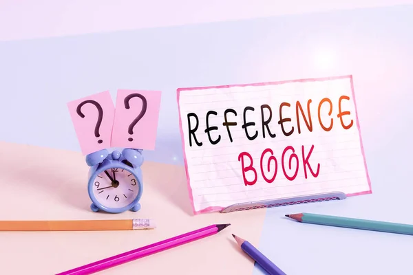 Text sign showing Reference Book. Conceptual photo book to be consulted for information on specific matters Mini size alarm clock beside stationary placed tilted on pastel backdrop.