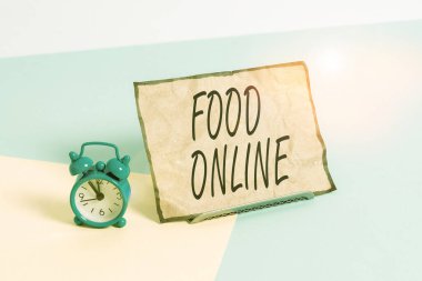 Conceptual hand writing showing Food Online. Business photo text most convenient way for customers to purchase food online Alarm clock beside a Paper sheet placed on pastel backdrop.