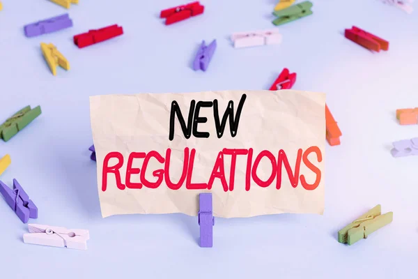 Text sign showing New Regulations. Conceptual photo rules made government order control something done Colored clothespin papers empty reminder blue floor background office pin.