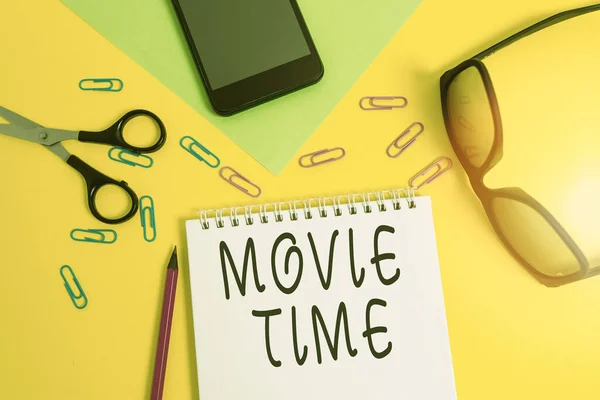 Writing note showing Movie Time. Business photo showcasing the scheduled or actual time at which a show or film begins Sheet pencil smartphone scissors eyeglasses notepad color background. — Stockfoto