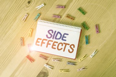 El yazısı Yan Efektleri. Bir ilaç veya tıbbi tedavinin istenmeyen ikincil etkisi anlamına gelen kavram. Renkli çamaşır iğnesi kağıtları boş ahşap zemin ofisini anımsatıyor..